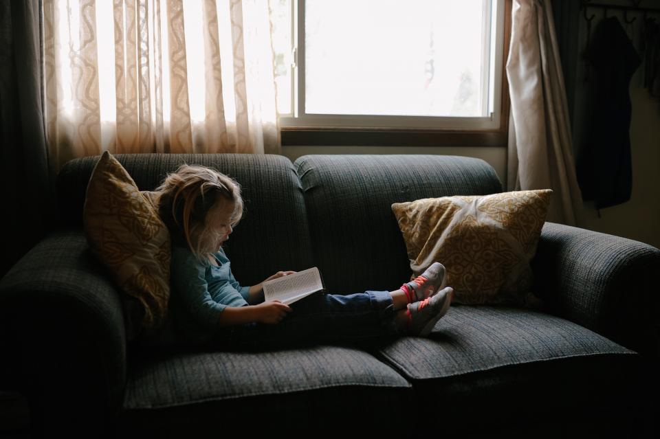 Enfant lisant un livre sur un canape pres d une fenetre